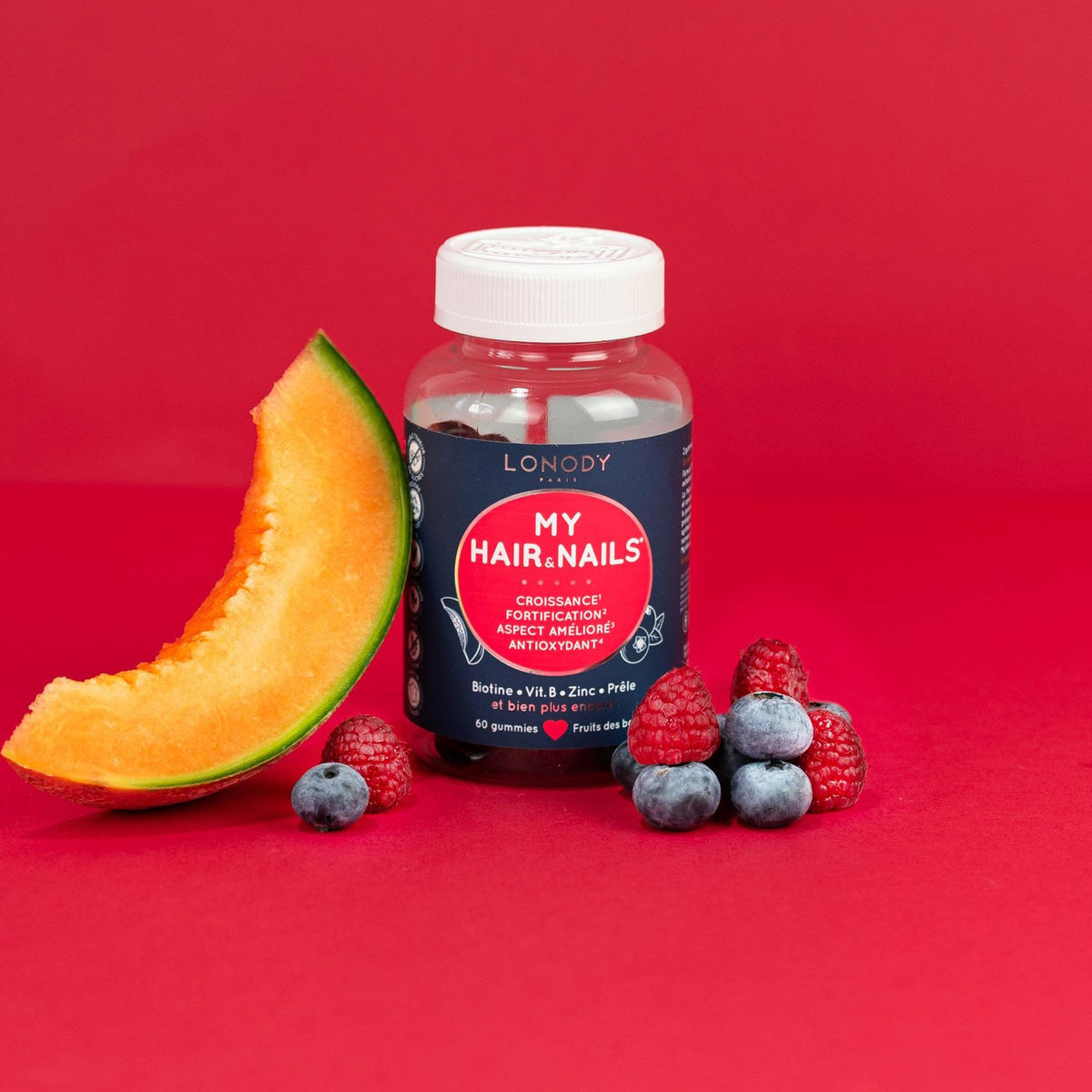 Flacon de gummies sans sucre MY HAIR & NAILS de Lonody avec melon, framboises et myrtilles sur fond rouge